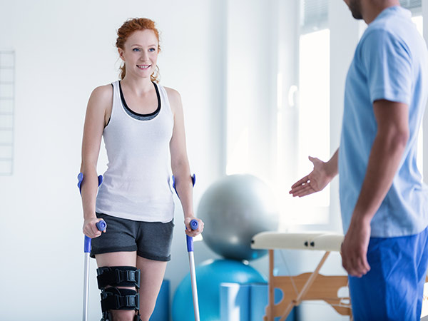 Girl walking on crutches towards physical therapist.