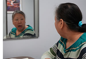 Woman looking in mirror as she forms words with her mouth.